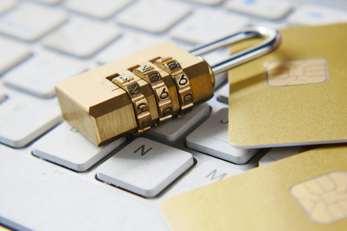 Gold combination padlock on a keyboard with credit cards, representing digital security and cryptographic key management in bridge infrastructure
